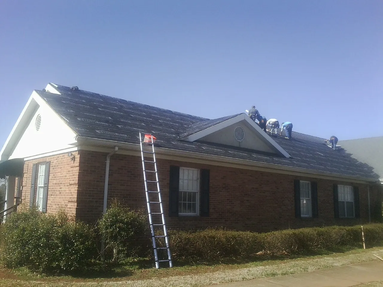 Crew tearing shingles off a brick ranch roof with a ladder set — Emergency Roof Repair work by our crew in Wilmerding