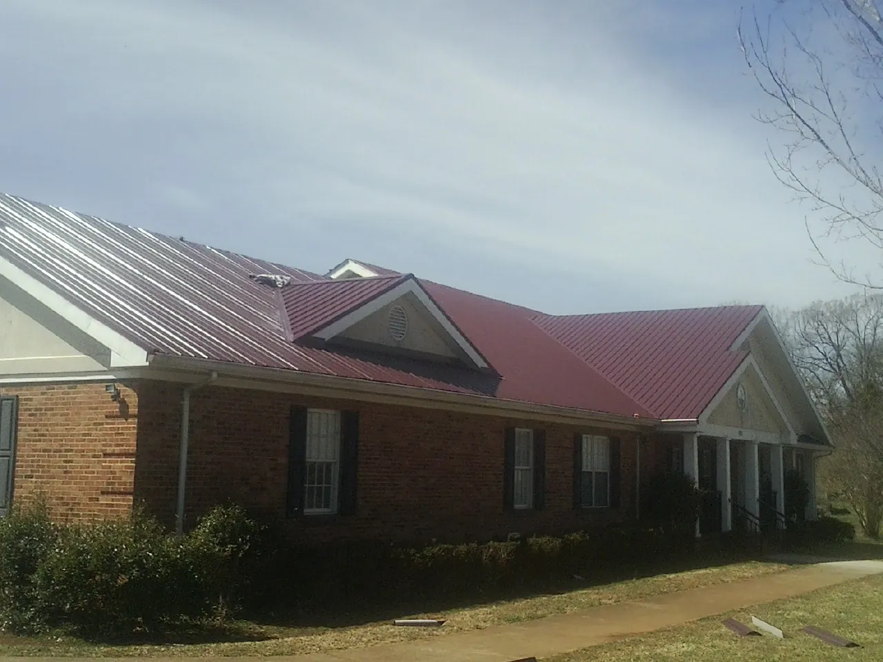 Red metal roof with gabled entries on a long brick building, from a Hail Damage Roof Repair job in Wilmerding