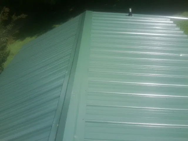 New green metal panels meeting at the ridge of a roof — Flat Roof Repair work by our crew in Wilmerding