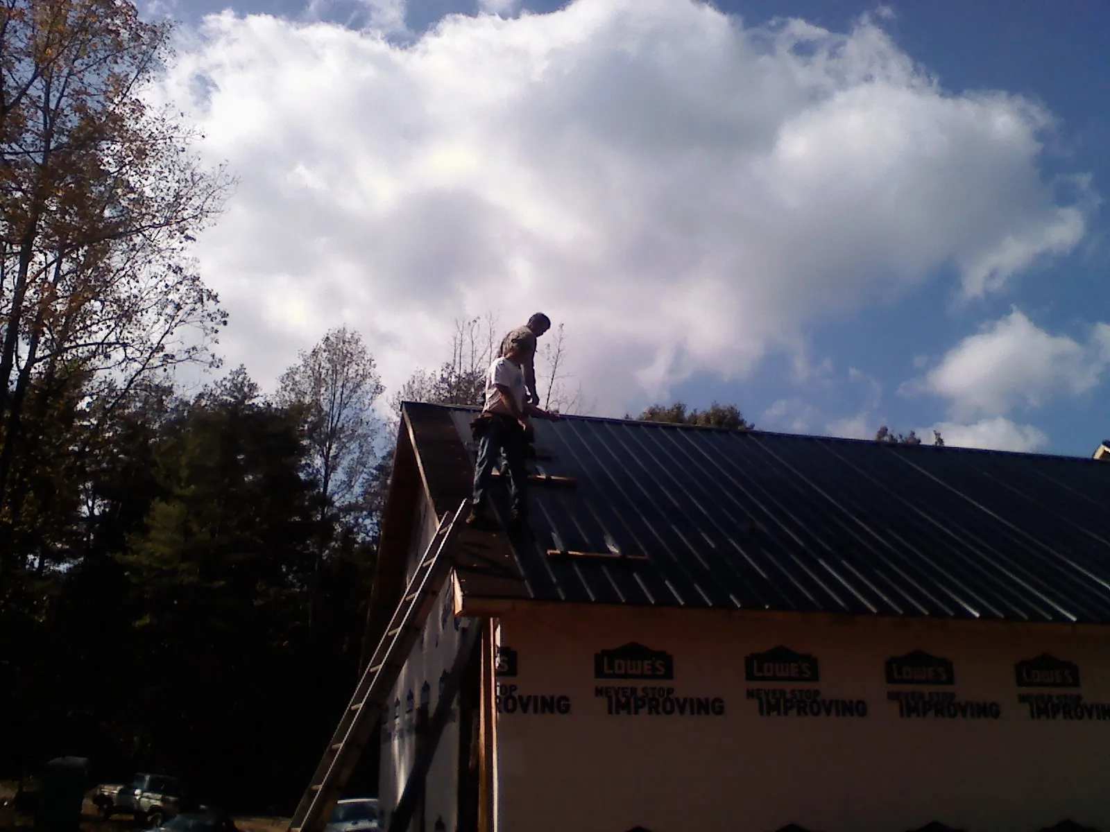 Roofer fastening dark metal panels high against a cloudy sky, from a Roof Inspection job in Wilmerding