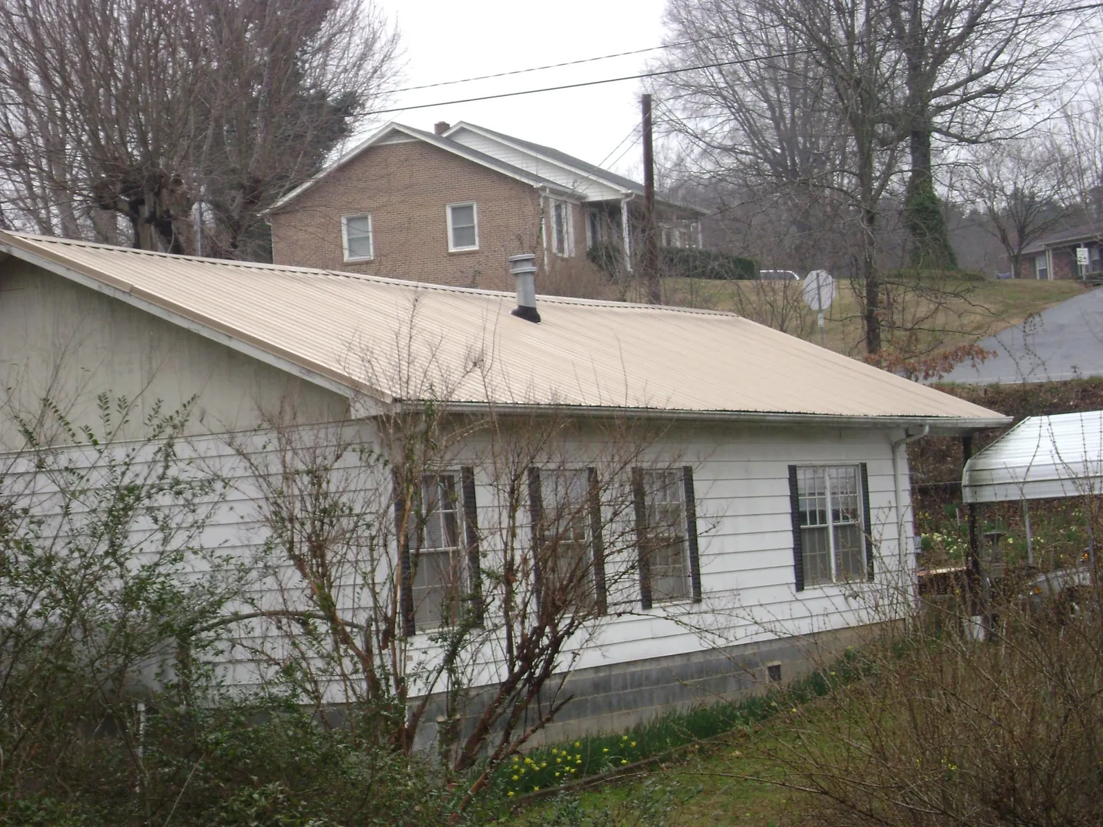 Tan metal roof on a white sided house set into a hillside — Commercial Roofing by Roofing Brothers in Wilmerding